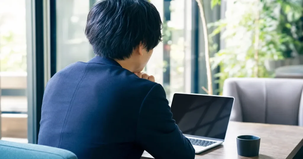 窓の外を見つめながらキャリアについて悩むスーツ姿の男性