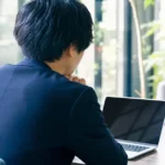 窓の外を見つめながらキャリアについて悩むスーツ姿の男性