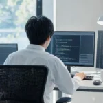 背中越しにコードを書くITエンジニアの作業風景